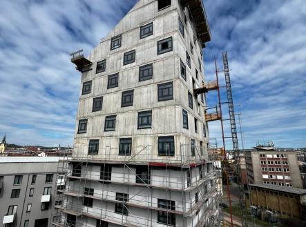 Nově budovaná bytová budova s moderním designem, betonovým povrchem a velkými okny, nacházející se v rozvíjející se městské lokalitě. | Prodej bytu, 3+kk, 100 m²