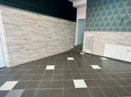 Prostor s dlažbou a dekorativní tapetou, vhodný pro rekonstrukci. Světlé stěny a designový prvek nabízí moderní možnosti využití. | Pronájem - obchodní prostor, 35 m²
