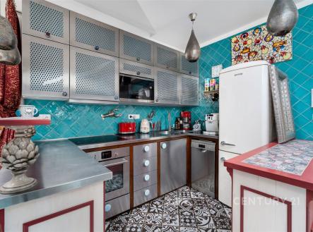 Kompaktní kuchyň s modrými dlaždicemi, nerezovými spotřebiči a dekorativními obklady. Retro lednice a mozaiková podlaha dodávají vintage styl. | Prodej bytu, 3+kk, 80 m²