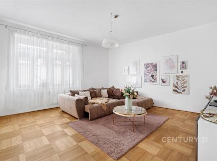 Světlý obývací pokoj s parketovou podlahou, moderní dekorací a velkými okny, poskytující prostorný a útulný interiér. | Prodej bytu, 5+kk, 146 m²