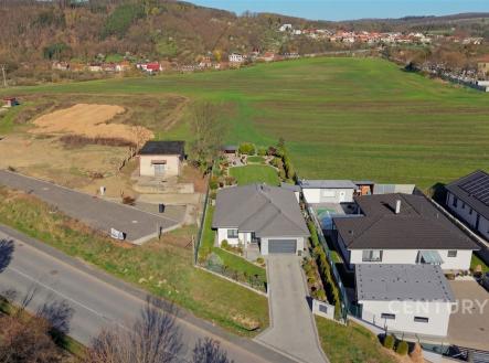 Pohled na moderní rodinný dům s velkými okny a zahradou, nacházející se v klidné oblasti s výhledem na louku a okolní krajinu. | Prodej - pozemek pro bydlení, 1 150 m²