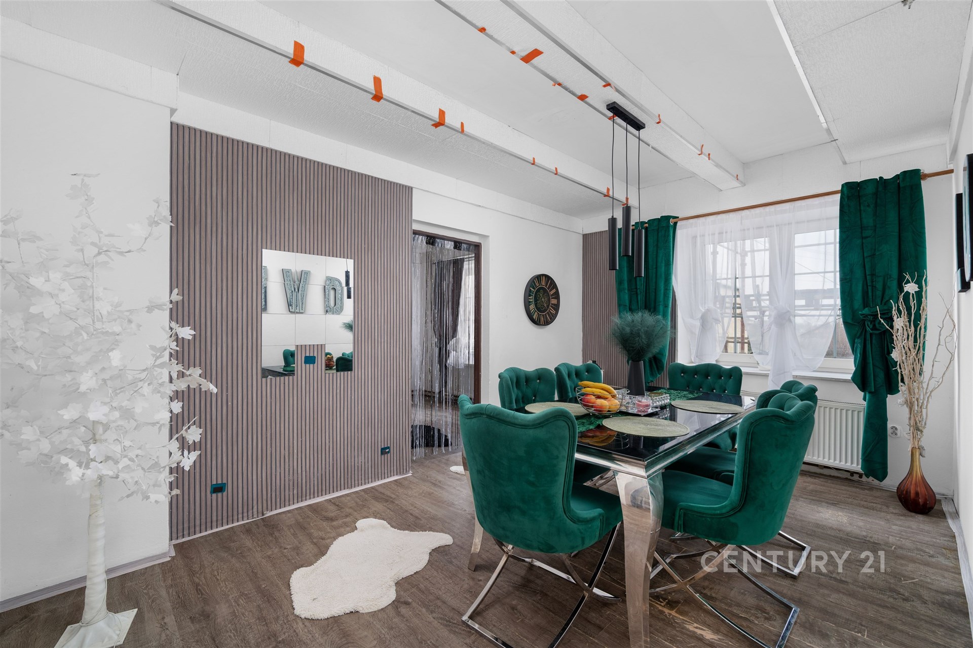 Jídelna s moderním designem, luxusní zelené čalounění, tmavá dřevěná podlaha, velká okna se závěsy, elegantní osvětlení, světlý interiér.