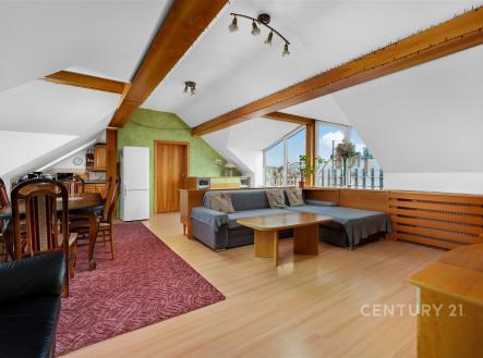 Podkrovní obývací pokoj s parketovou podlahou a velkými okny, moderní kuchyňský kout a dřevěné stropní trámy, světlý a prostorný prostor. | Prodej bytu, 3+kk, 127 m²