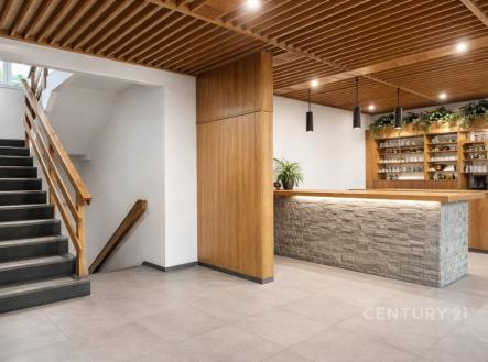 Recepční prostor s moderním designem, dřevěným obložením a kamenným pultem, doplněný kovovými svítidly a parketovou podlahou pro stylový vzhled. | Prodej - dům/vila, 170 m²