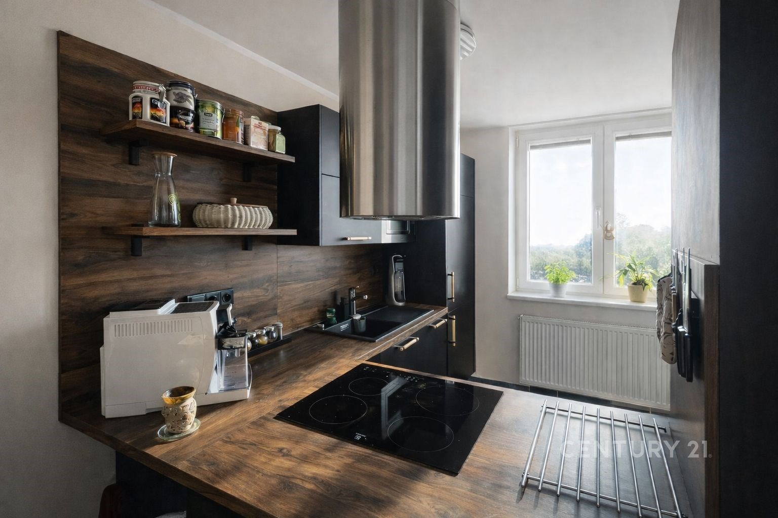 Moderní kuchyň s dřevěnou linkou a velkými okny, která propouštějí dostatek světla, doplněná elegantními černými spotřebiči.