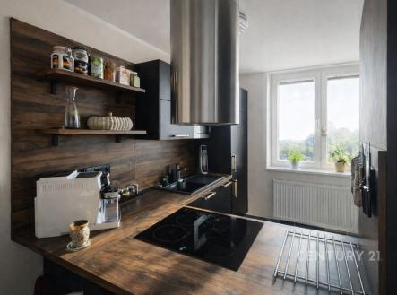 Moderní kuchyň s dřevěnou linkou a velkými okny, která propouštějí dostatek světla, doplněná elegantními černými spotřebiči. | Prodej bytu, 2+kk, 54 m²