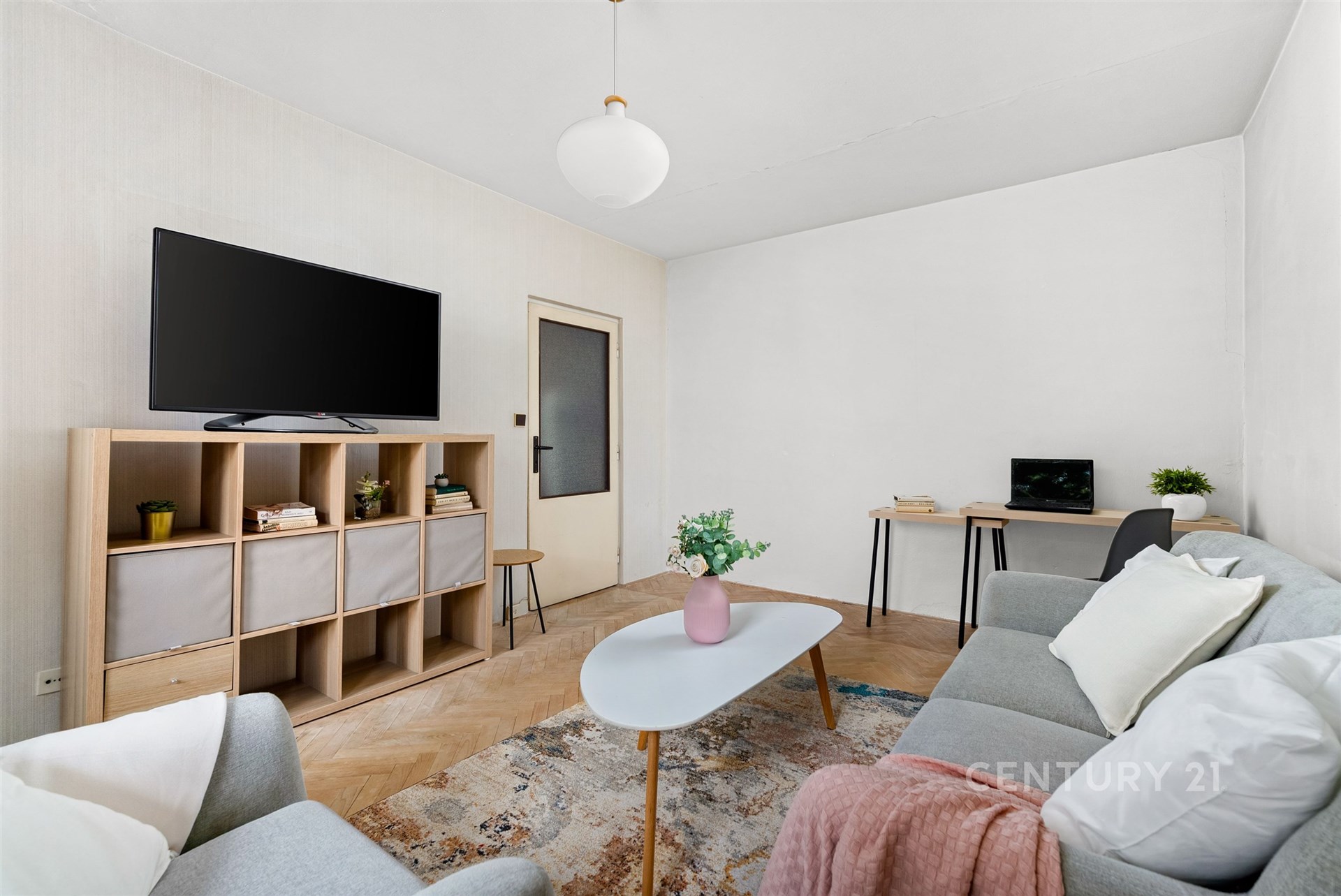 Světlý obývací pokoj s parketovou podlahou, moderním nábytkem a velkým oknem, poskytující útulný prostor pro relaxaci a práci.