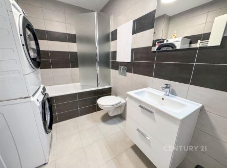 Moderní koupelna s dlažbou, vestavěným umyvadlem a úložnou skříňkou. Kombinace světlých a tmavých obkladů, pračka se sušičkou. | Pronájem bytu, 1+kk, 36 m²