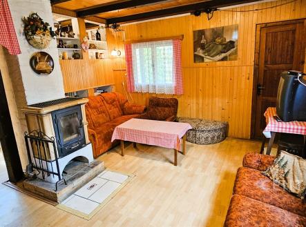 Útulný obývací pokoj s dřevěnými obklady, krbovými kamny a parketovou podlahou, nabízí rustikální atmosféru a tradiční design. | Prodej - chata/rekreační objekt, 50 m²