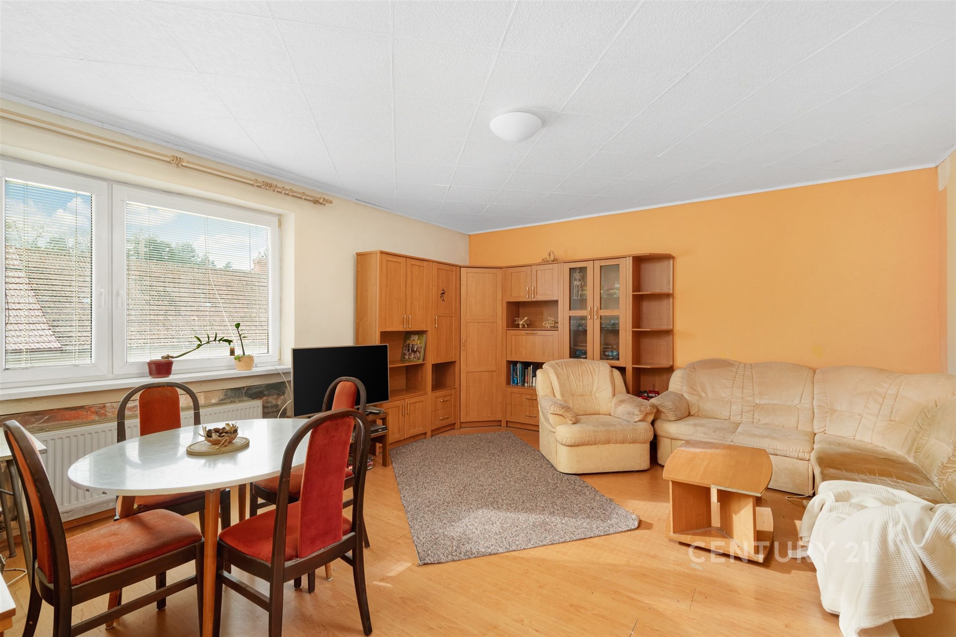 Světlý obývací pokoj s parketovou podlahou, velkou rohovou sedačkou a dřevěným nábytkem. Útulný interiér s velkými okny.