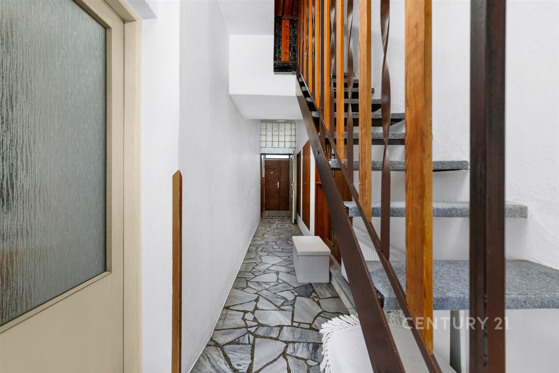 Chodba s kameninovou dlažbou, dřevěným zábradlím a vstupními dveřmi. Funkční design a přírodní materiály přinášejí moderní pocit.