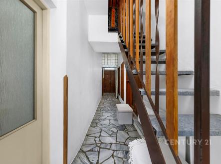 Chodba s kameninovou dlažbou, dřevěným zábradlím a vstupními dveřmi. Funkční design a přírodní materiály přinášejí moderní pocit. | Prodej - dům/vila, 84 m²