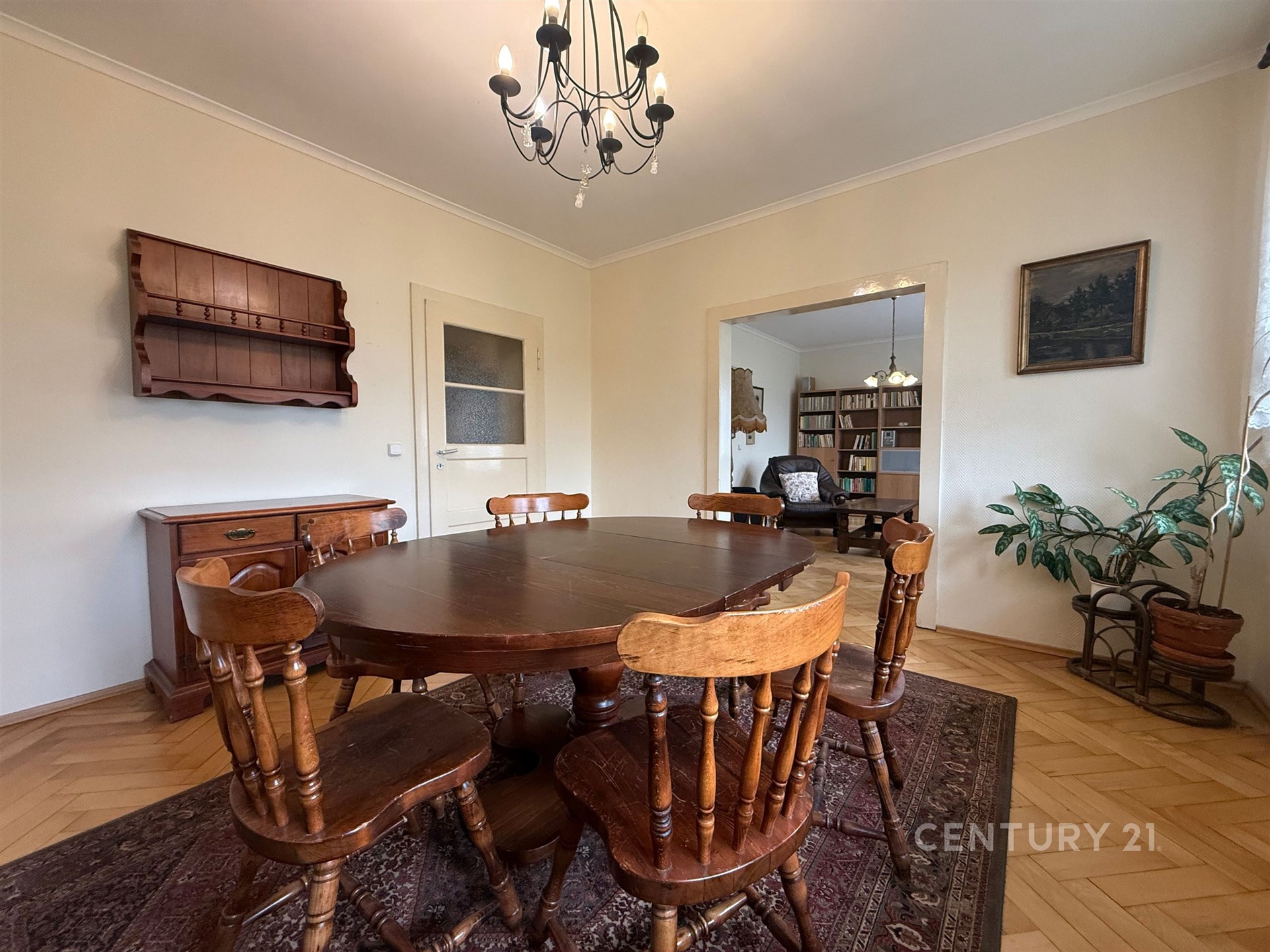 Jídelna s parketovou podlahou, dřevěným nábytkem a světlými stěnami, doplněná vestavěnými skříněmi a klasickým lustrem.