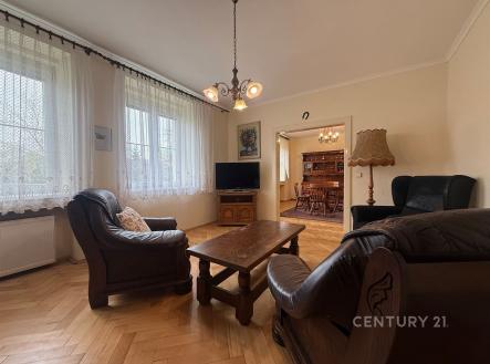 Světlý obývací pokoj s parketovou podlahou, velkými okny a koženým nábytkem, propojený s jídelnou, vytváří útulný a elegantní prostor. | Prodej bytu, 5+1, 110 m²