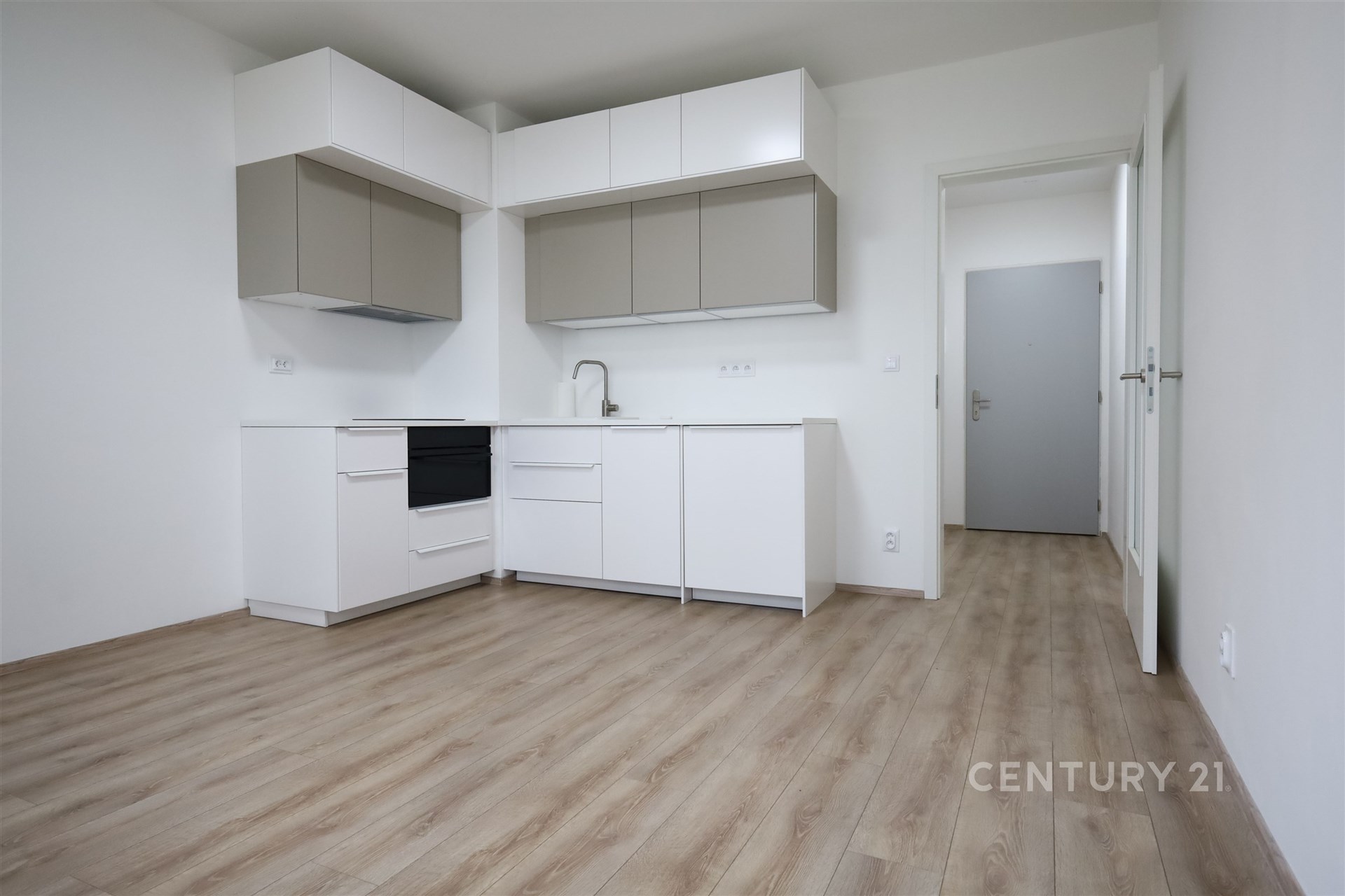 Moderní kuchyň s parketovou podlahou, světlé skříňky a vestavěné spotřebiče v nově rekonstruovaném bytě.