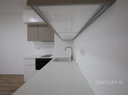 Moderní kuchyň s bílými skříňkami, vestavěnou troubou a dřezem, parketová podlaha ladí s minimalistickým designem. | Pronájem bytu, 1+kk, 27 m²