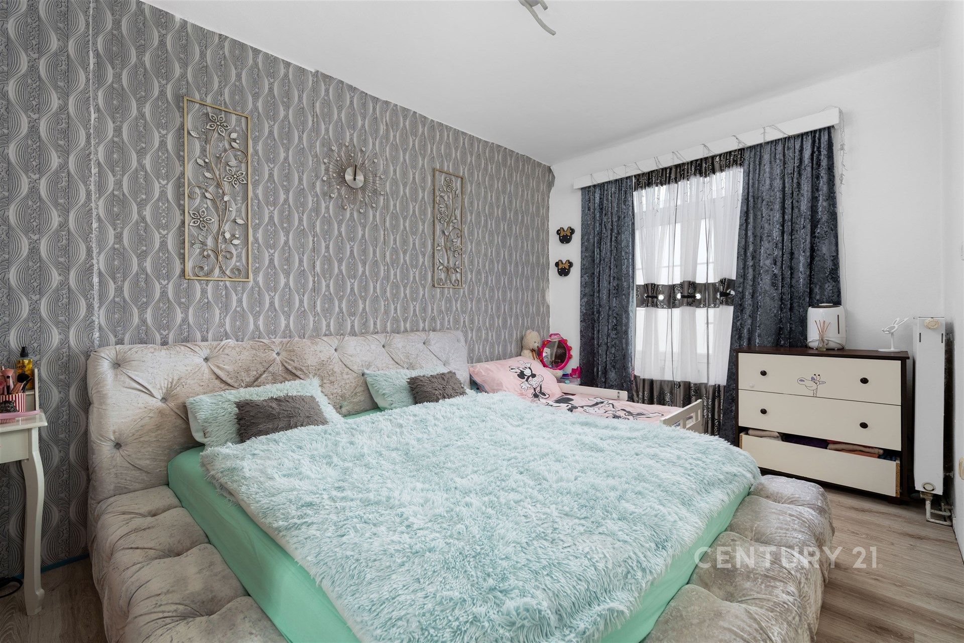 Prostorná ložnice s parketovou podlahou, moderní tapetou a velkými okny přinášejícími dostatek světla, nabízí stylový a pohodlný interiér.