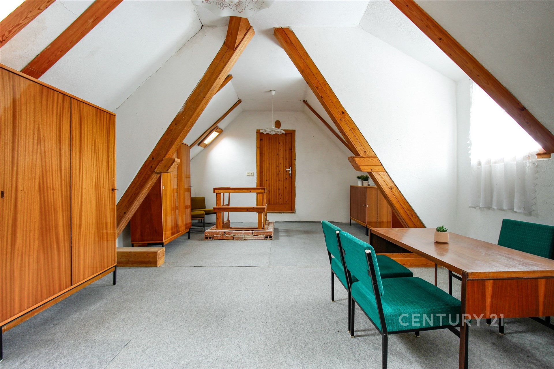 Podkrovní obývací pokoj s retro nábytkem, dřevěnými trámy a světlými stěnami. Výrazná dřevěná lamelová skříň a konferenční stolek.