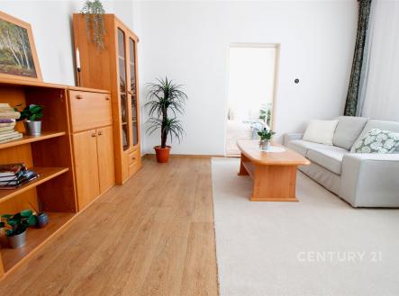 Světlý obývací pokoj s dřevěnými skříněmi, parketovou podlahou a velkými okny, doplněný moderním světlým nábytkem a zelenými rostlinami. | Prodej - dům/vila, 124 m²