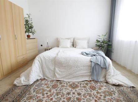 Prostorná ložnice s parketovou podlahou, velkými okny a světlou výmalbou, doplněná moderním nábytkem a dekorativním kobercem. | Prodej - dům/vila, 124 m²