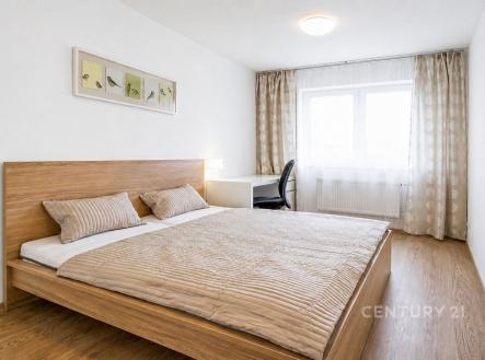 Moderní ložnice s dřevěnou podlahou, velkým oknem a světlým interiérem, vybavená pracovní stůlcem a elegantní dekorací na stěně. | Prodej bytu, 2+kk, 54 m²