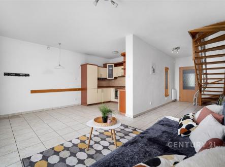 Obývací pokoj s moderní dlažbou, dřevěným schodištěm a světlou kuchyní. Velká okna umožňují přirozené světlo a vytváří prostorný dojem. | Prodej - dům/vila, 90 m²