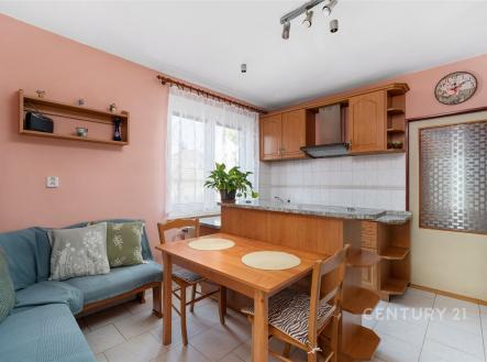 Kuchyňský kout s moderní dřevěnou linkou a světlou dlažbou, vedle jídelního stolu se nachází pohodlná sedací souprava, velké okno zajišťuje dostatek světla. | Prodej - dům/vila, 227 m²