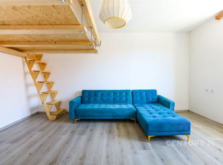 Obývací pokoj s modrou rohovou sedačkou, světlou parketovou podlahou a dřevěným schodištěm, moderní design a velká okna přinášejí dostatek světla. | Prodej bytu, 1+1, 40 m²