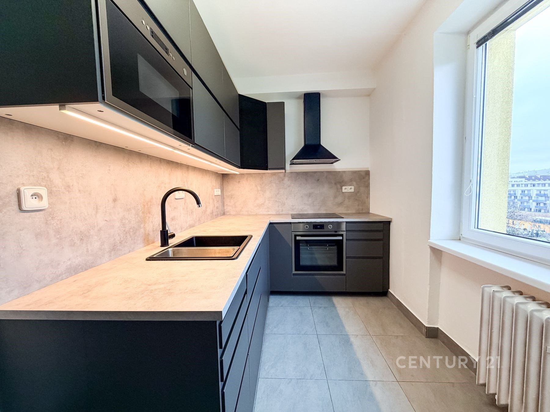 Moderní kuchyň s tmavými skříňkami, vestavěnými spotřebiči a světlou dlažbou, nabízí elegantní design a současné vybavení.