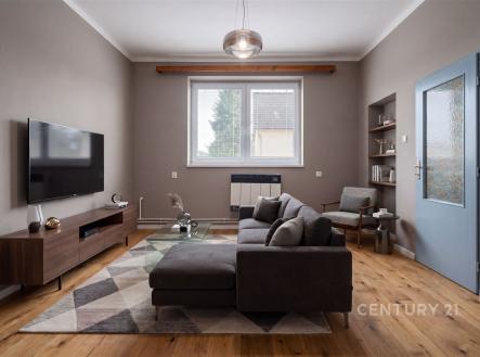 Světlý obývací pokoj s parketovou podlahou, moderní sedačkou a velkým oknem. Elegantní styl doplňuje dřevěný televizní stolek a dekorativní koberec. | Prodej - dům/vila, 90 m²