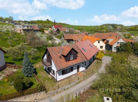 Rodinný dům s červenou střechou a dřevěným balkonem, obklopený zahradou, v klidné vesnické lokalitě s výhledem na okolní kopce. | Prodej - chata/rekreační objekt, 150 m²