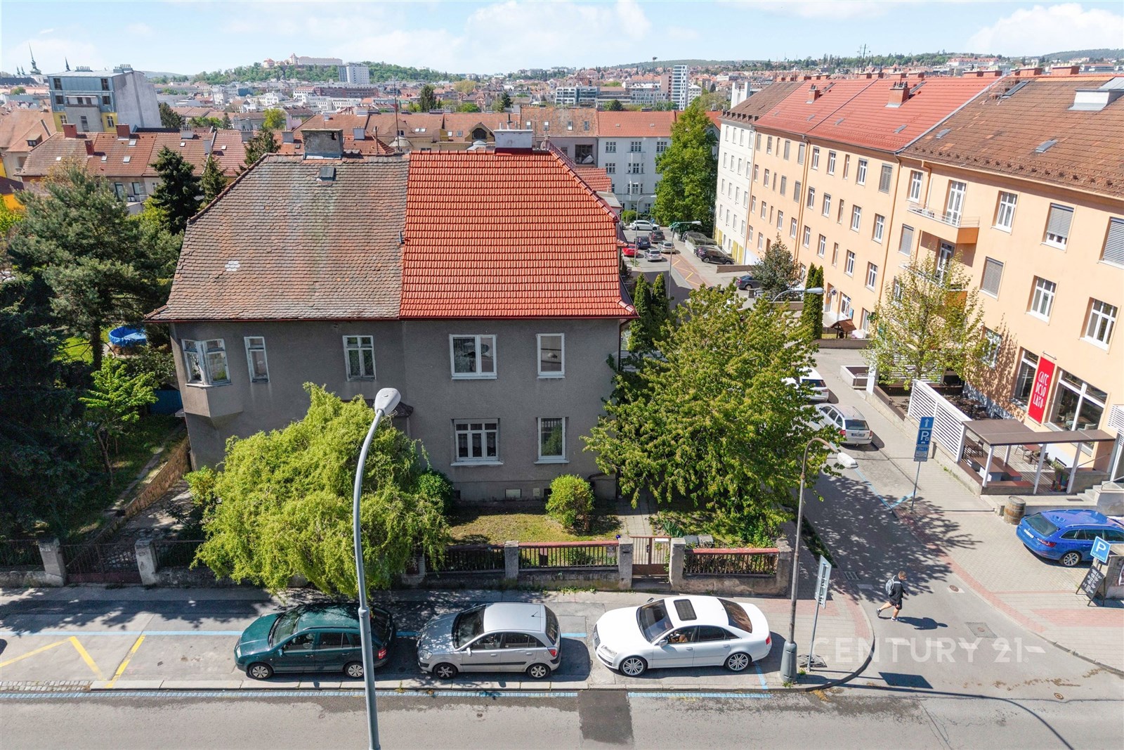 Prázdný venkovní prostor s rodinným domem, červenou střechou a zahradou, obklopený městskou infrastrukturou.