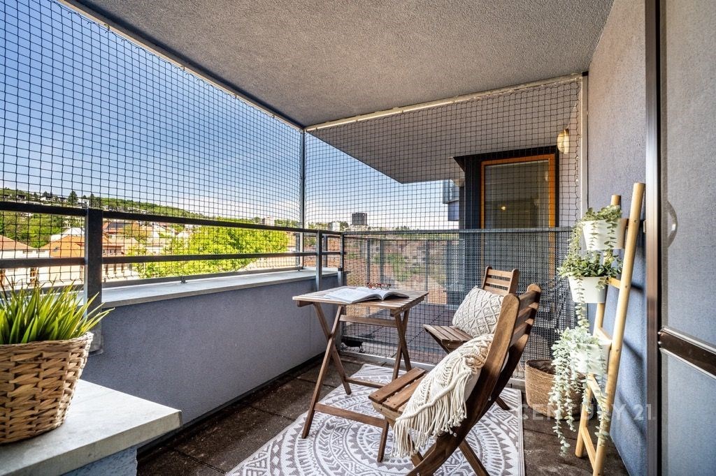Zastřešený balkon s dřevěným nábytkem, moderní dlažbou a výhledem na město, ideální místo k relaxaci.