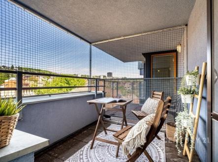 Zastřešený balkon s dřevěným nábytkem, moderní dlažbou a výhledem na město, ideální místo k relaxaci. | Prodej bytu, 1+kk, 37 m²