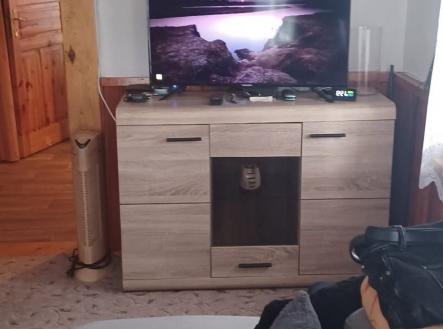 Obývací pokoj s moderním nábytkem, dřevo dekorem a velkou televizí, světlý prostor s přístupem do sousedního pokoje. | Prodej - dům/vila, 120 m²