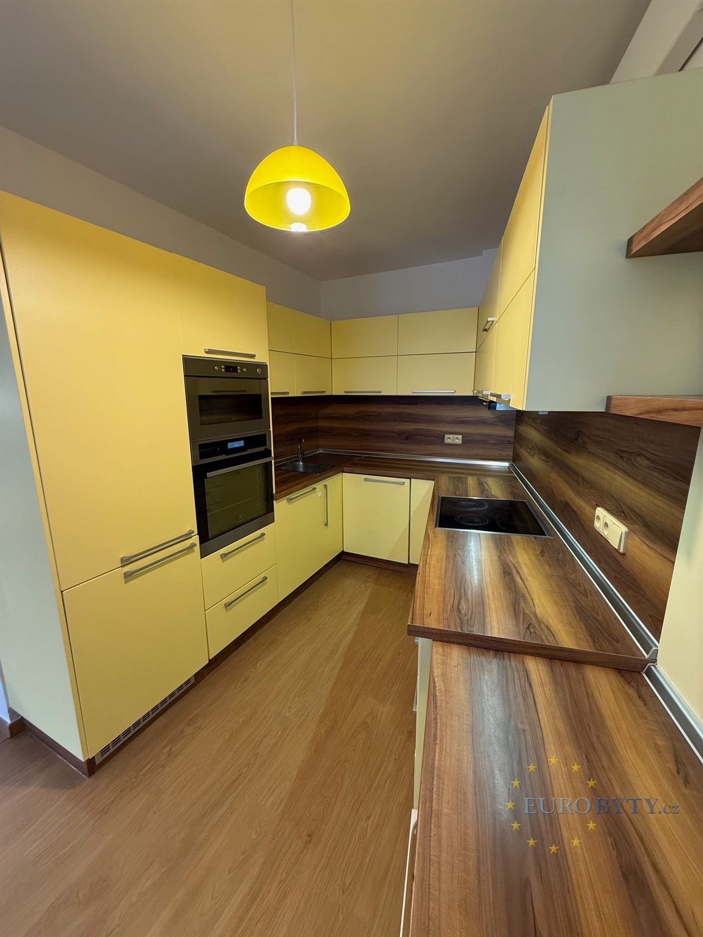 Moderní kuchyň s dřevěnou pracovní deskou, vestavěnými spotřebiči a parketovou podlahou. Světlé skříňky poskytují dostatek úložného prostoru.