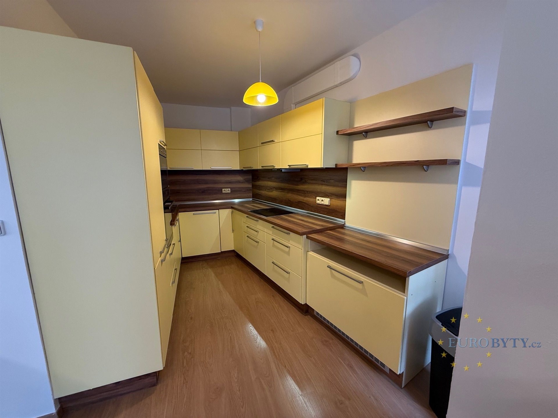 Moderní kuchyň s dřevěnou podlahou, světlými skříňkami a vestavěnými úložnými prostory, vybavená moderními spotřebiči.