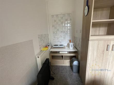 Malá kuchyň s dlažbou, dřevěnou skříňkou a elektrickým radiátorem, vhodná pro garsoniéru nebo menší byt. | Pronájem bytu, garsoniéra, 12 m²