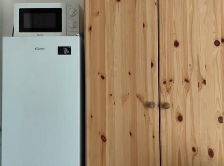 Kuchyň s lednicí, mikrovlnnou troubou a dřevěnými vestavěnými skříněmi, moderní vzhled a dlažba na podlaze pro snadnou údržbu. | Pronájem bytu, garsoniéra, 12 m²