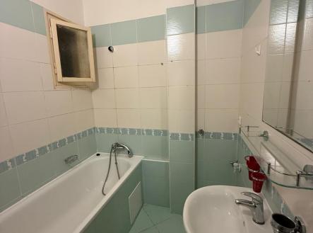 Koupelna s vanou, dlažbou a světlými obklady, vybavená umyvadlem a zrcadlem. Světlé stěny dodávají prostoru moderní vzhled. | Pronájem bytu, 1+kk, 35 m²