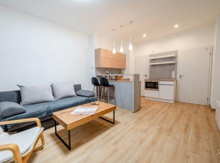 Světlý obývací pokoj s moderní kuchyní, parketová podlaha, velká okna, moderní styl, dřevěný nábytek, pohodlné sezení, otevřený prostor. | Pronájem bytu, 1+kk, 29 m²
