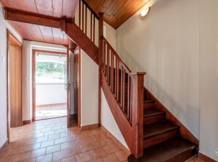 Chodba s dřevěným schodištěm, dlažba na podlaze, světlé stěny. Vstup do domu s přírodními materiály, prostorný a dobře osvětlený prostor. | Prodej - chata/rekreační objekt, 150 m²