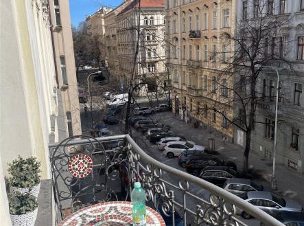 Balkon s kovaným zábradlím nabízí výhled na historické budovy. Stoleček s mozaikou dodává prostoru starosvětský šarm. | Pronájem bytu, 3+kk, 108 m²