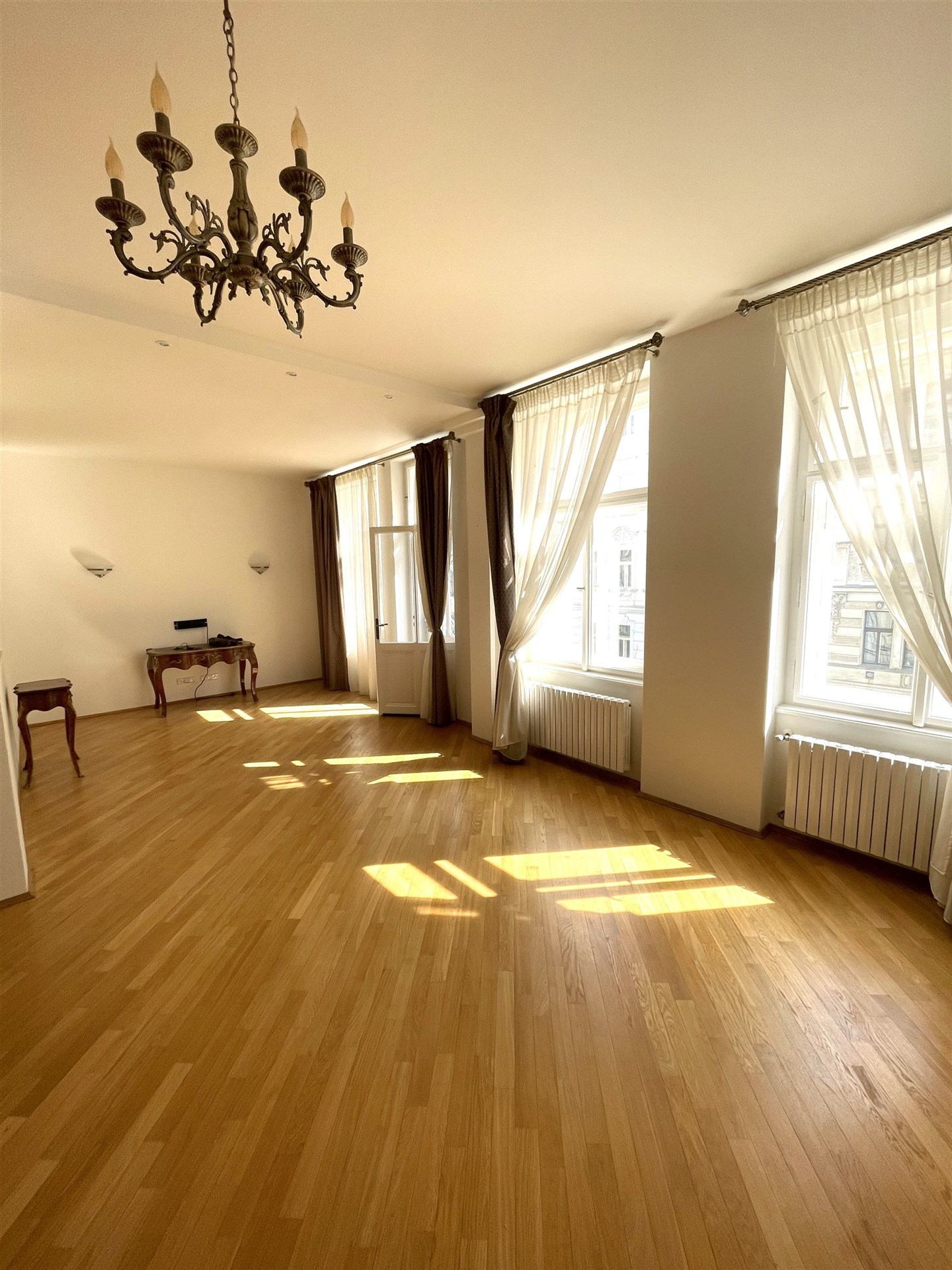 Světlý obývací pokoj s parketovou podlahou, velká okna s dlouhými závěsy, historický lustr, renovovaný interiér stylového bytu