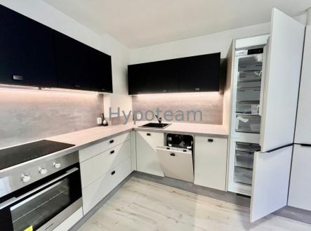 Moderní kuchyň s vestavěnými spotřebiči, světlou dřevěnou podlahou a tmavými horními skříňkami. | Pronájem bytu, 2+kk, 55 m²