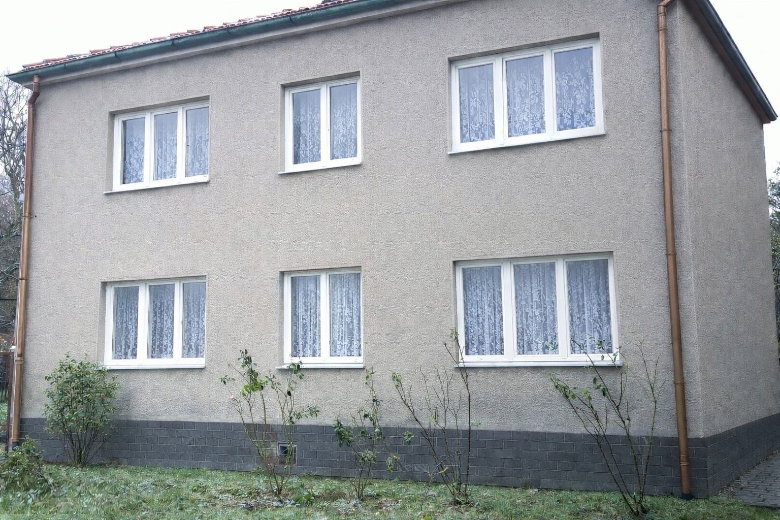 Dvoupatrový rodinný dům s novými okny, šedou omítkou a zahradou, nacházející se v klidné lokalitě, vhodný pro rekonstrukci.