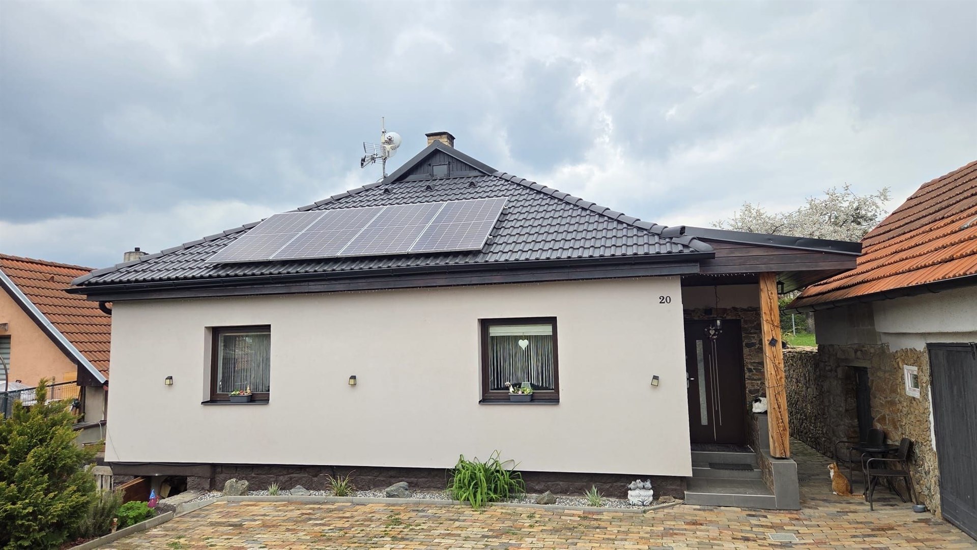 Moderní rodinný dům s černou střešní krytinou a solárními panely, dlažba na příjezdové cestě, světlá fasáda, kvalitní izolace