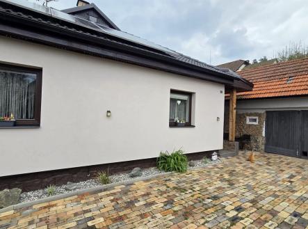 Fasáda rodinného domu s moderními okny, vydlážděným dvorem a dřevěnou garáží nabízí atraktivní kombinaci stylu a funkčnosti. | Prodej - dům/vila, 180 m²