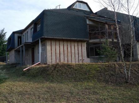 Exteriér neobydleného domu s šikmou střechou, částečně dokončenou fasádou a oplocenou zahradou, vhodný k rekonstrukci. | Prodej - dům/vila, 925 m²