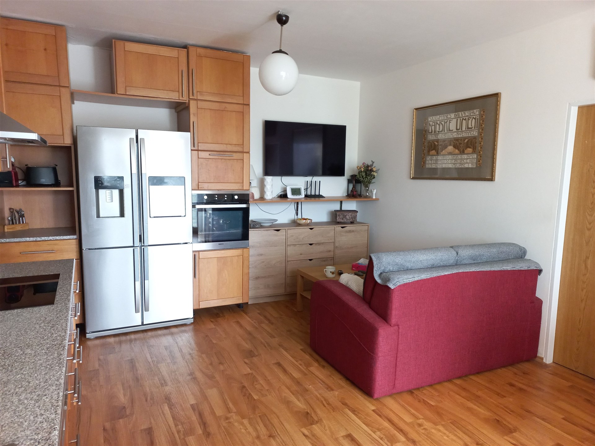 Kuchyň s obývacím prostorem, parketová podlaha, moderní skříňky, vestavěné spotřebiče, světlý interiér, prostorná lednice, pohodlná sedačka.